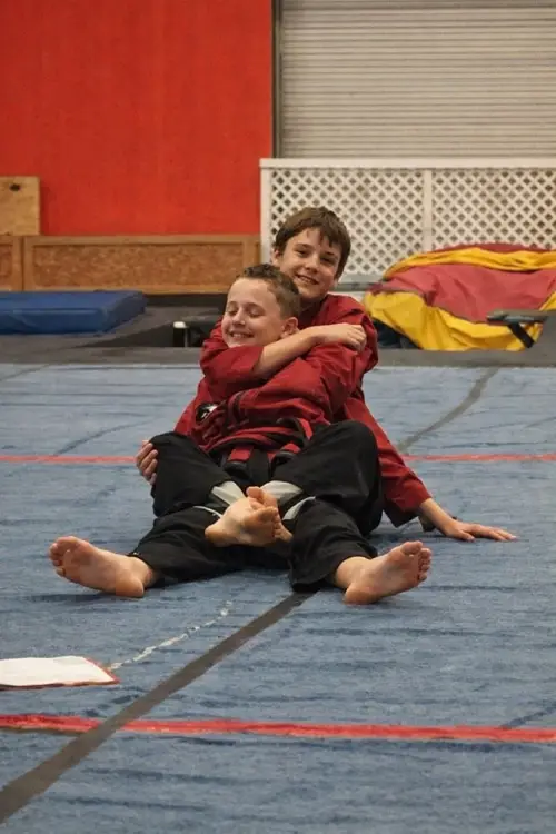 Two kids smiling and resting on the mat after jiu jitsu class in Waco TX